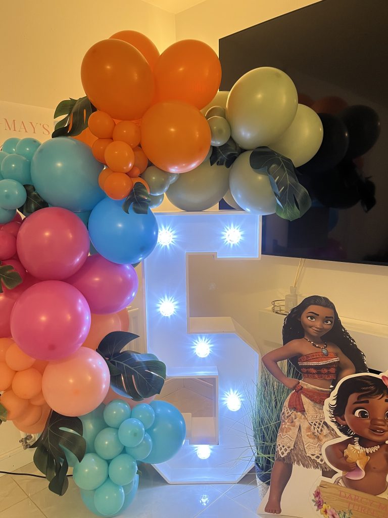 5th birthday light up number with multi-coloured balloons, leaves, and Moana cut-outs