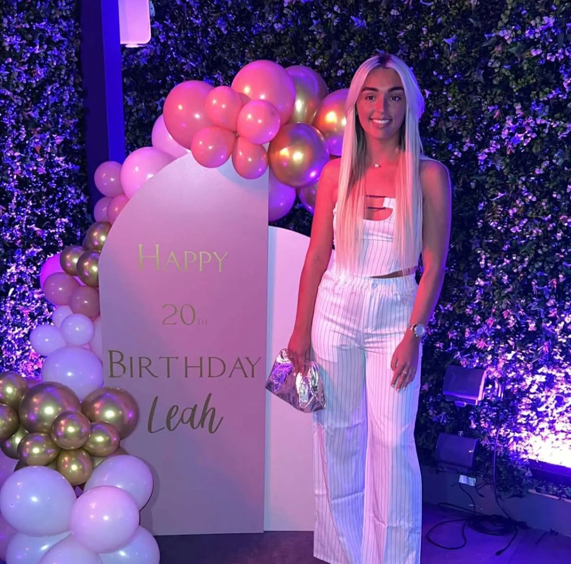 Girl standing in front of 20th birthday pink white and gold sign and balloon display